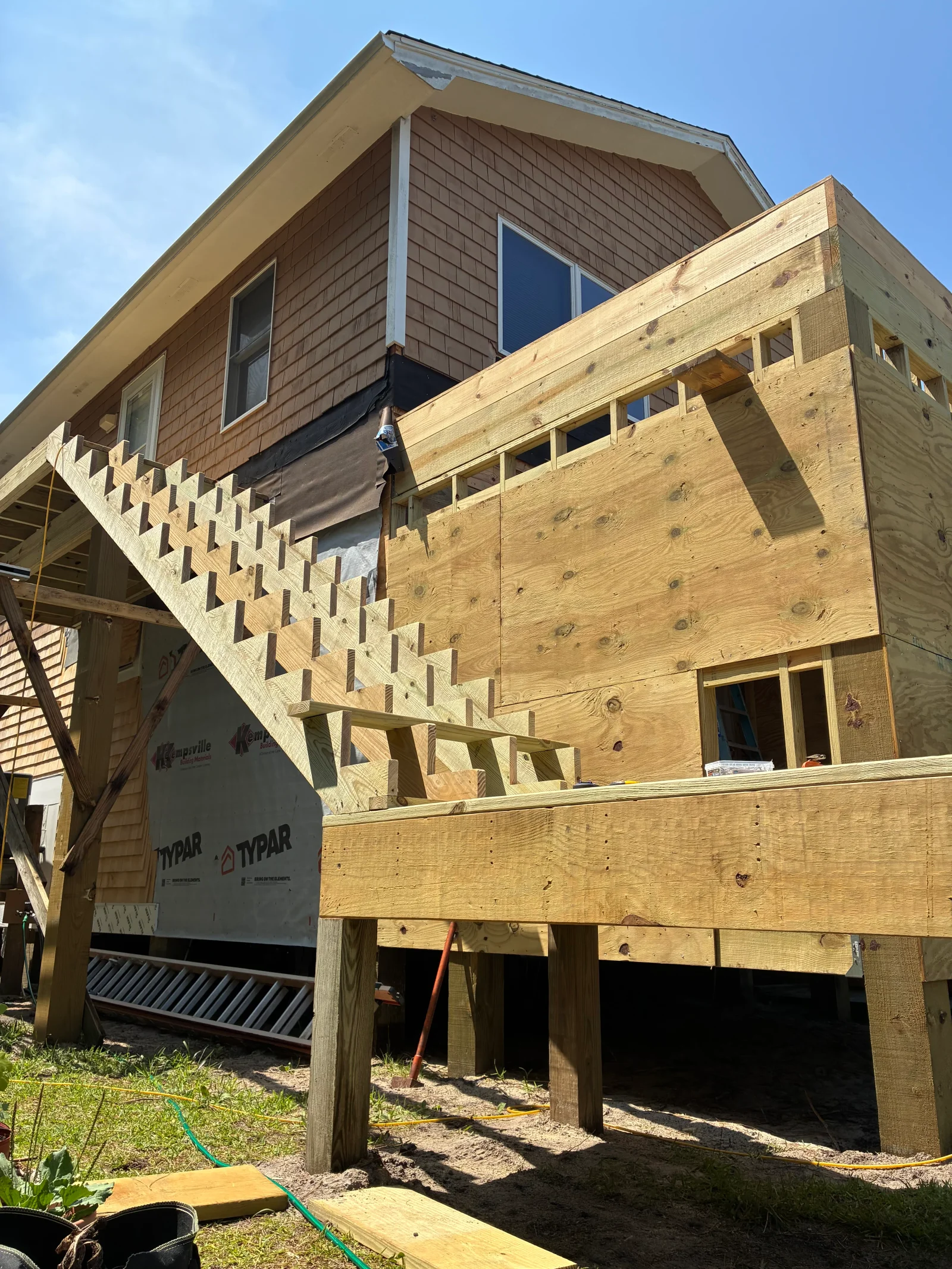 Framed elevated addition with pressure-treated posts, plywood sheathing, and open-riser wood staircase in progress