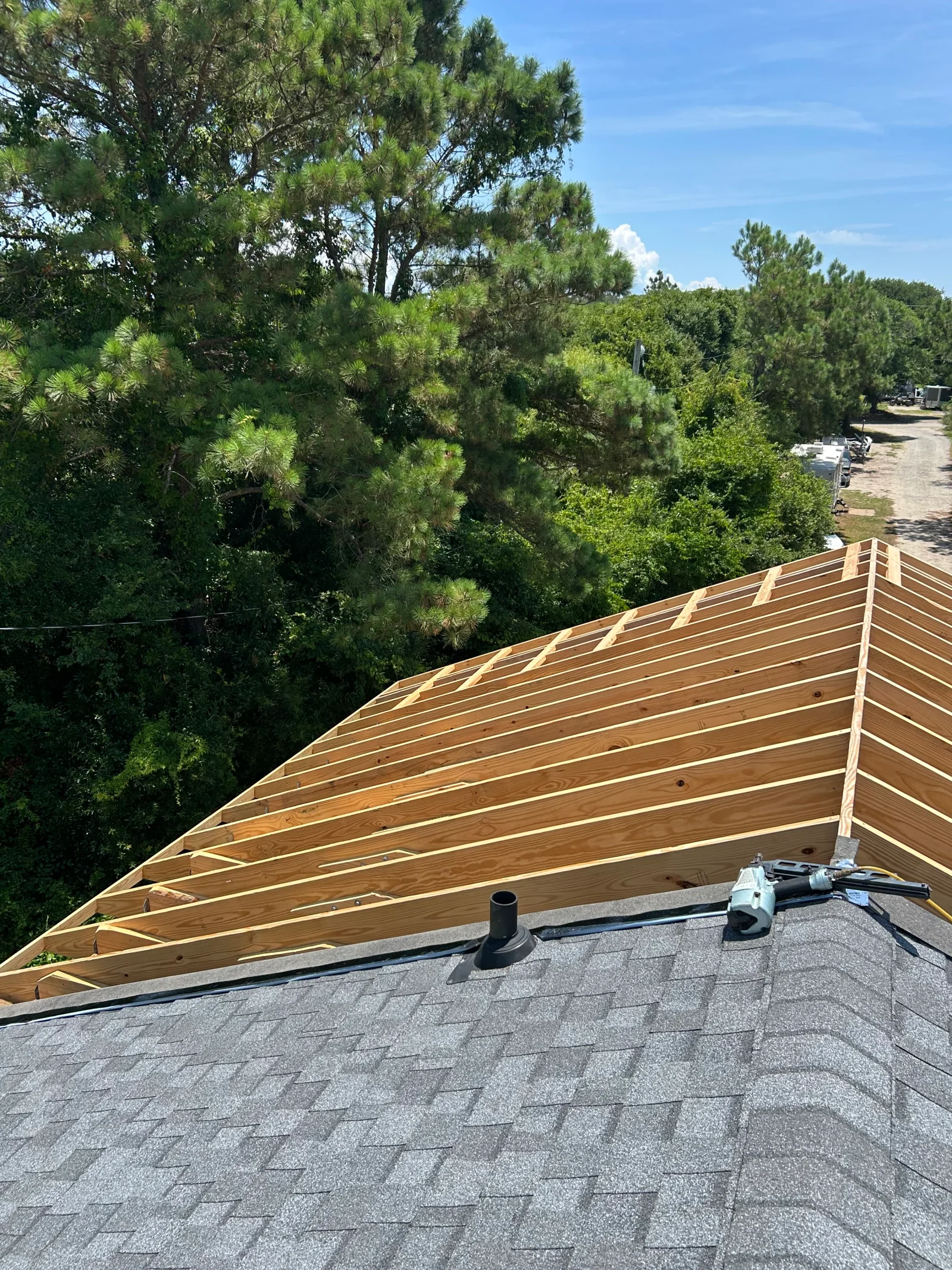 Exposed wood roof sheathing over rafters with dark gray asphalt shingles and a black vent pipe boot on a roofing project