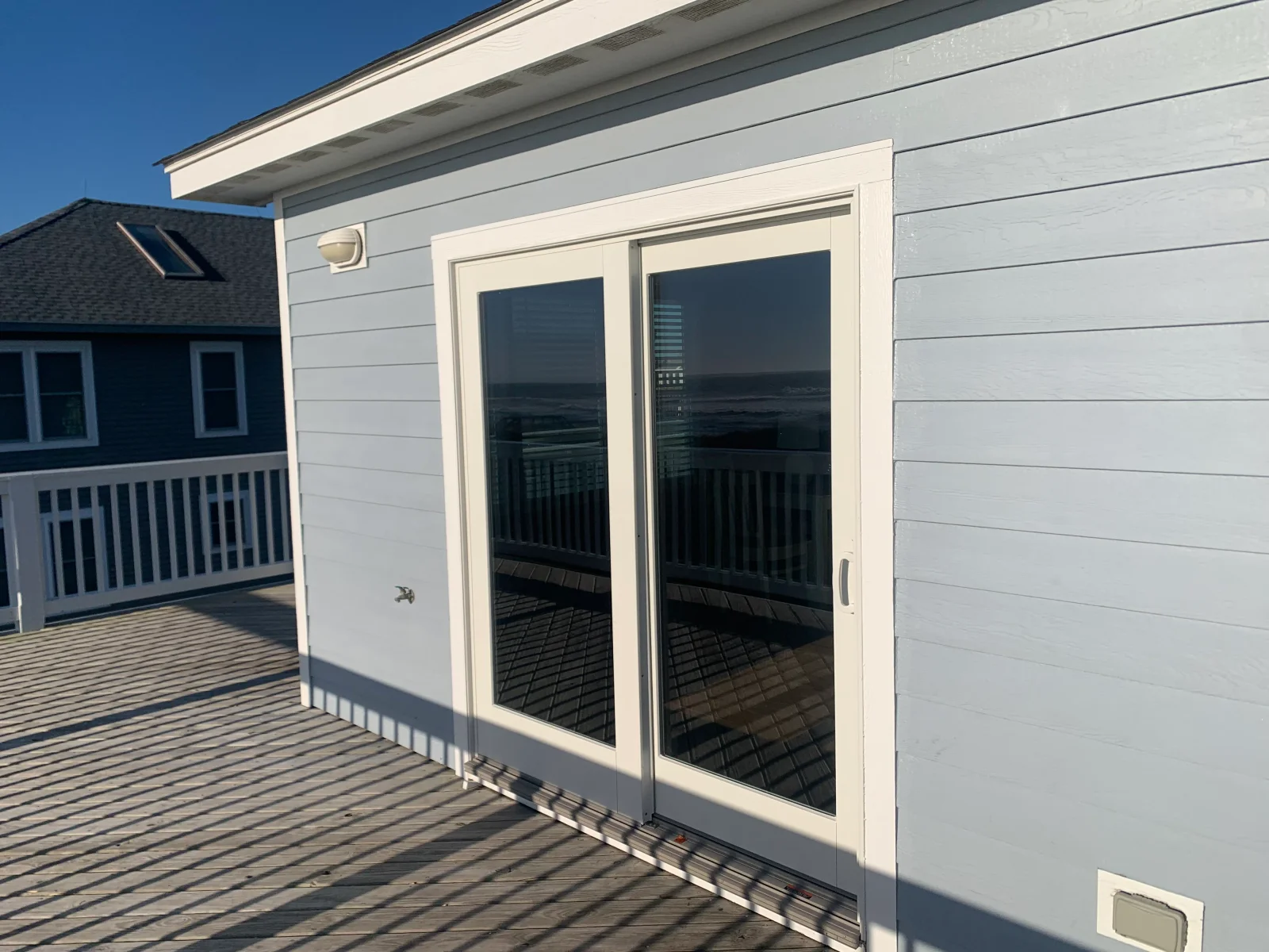 White sliding glass patio doors with trim set in light blue lap siding, opening onto a gray wood deck