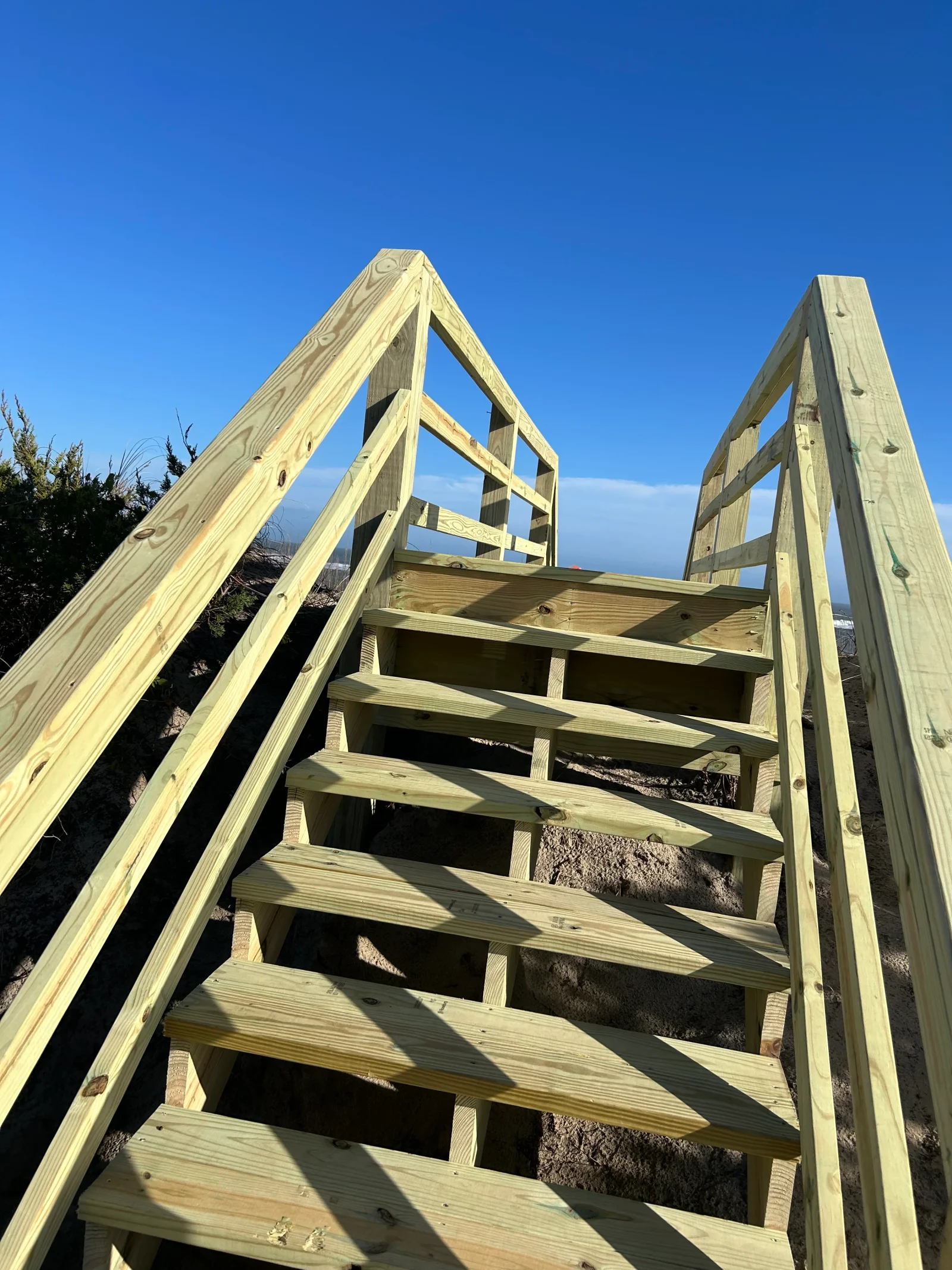 Pressure-treated pine dune staircase with open risers, stepped treads, and handrails built from dimensional lumber